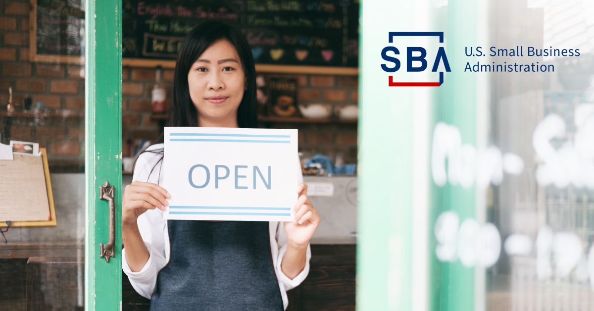 Small business owner standing in front of their shop holding an "Open" sign.